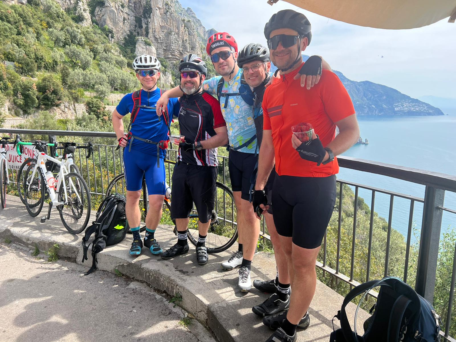 Group of five cyclists on a scenic overlook during a guided bike tour from Sorrento to Amalfi, with coastal cliffs and the sea in the background